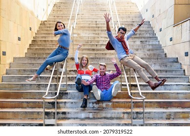 Multicultural group of happy excited friends cheering and laughing as they slide down the rails of a flight of external stairs in a city in a freedom and active lifestyle concept