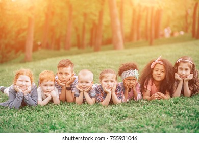 Multicultural Group Of Kids Friends At Meadow Resting On The Grass. The Concept Of Friendship, Childhood And Intercultural Communication.