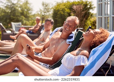 Multi-Cultural Group Of Senior Friends Relaxing On Sun Loungers By Outdoor Pool On Summer Vacation - Powered by Shutterstock