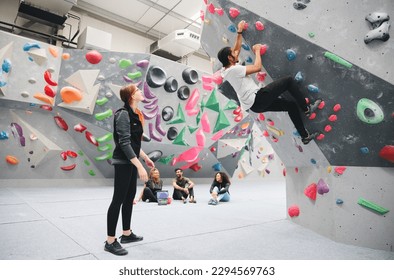 Multi-Cultural Group Watching Friend On Climbing Wall In Indoor Activity Centre With Coach - Powered by Shutterstock