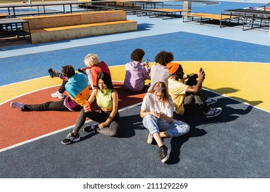 Multicultural group of young friends bonding outdoors and having fun - Stylish cool teens gathering at urban skate park and using smartphones and social media app