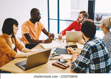 Multicultural Group Of Young People Dressed In Smart Casual Wear Discussing Planning Strategy Having Brainstorming Meeting In Office.Diverse Employees Collaborating On Organization Of Working Process