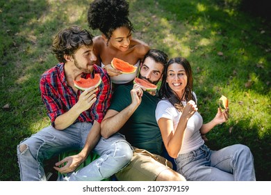 Multicultural Group Of Young People Eating Watermelon Sitting On The Grass In The Countryside