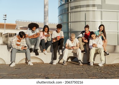Multicultural group of young trendy friends using cellphones and social media - Students sitting in modern urban area and typing on the smartphones - Shutterstock ID 2063750216