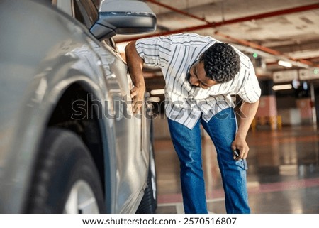 Multicultural man is looking at damage and scratch on car.