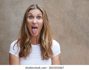 Multicultural Middle Aged Woman Making A Silly Face With Tongue Out While Looking At Camera With Raised Eyebrows                            