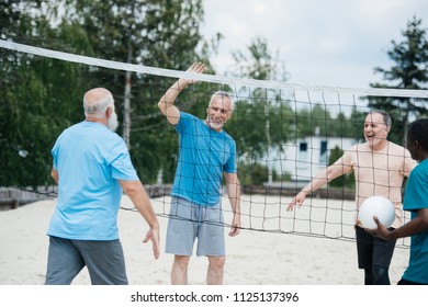 Multicultural Old Friends Playing Volleyball On Beach On Summer Day