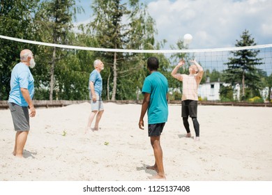 Multicultural Old Friends Playing Volleyball On Beach On Summer Day