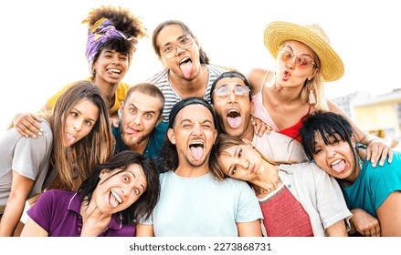 Multicultural people taking selfie sticking out tongue making funny faces - Genuine life style and integration concept with interracial young friends having fun together - Bright vivid filter - Shutterstock ID 2273868731