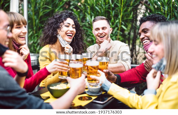 Multicultural people toasting beer wearing open\
face mask - New normal life style concept with friends having fun\
together at brewery bar garden - Warm filter with focus on woman in\
yellow clothes