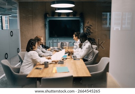 Multicultural professionals in casual breakout session, combining note-taking and digital device usage to capture ideas in creative, tech-oriented collaborative workspace