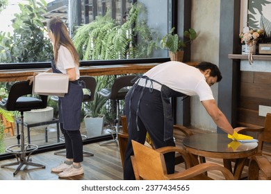 Multicultural small business man and woman cleaning restaurant coffee shop prepare open cafe, young barista couple Indian man and Asian woman wearing apron working in workplace make table for customer - Powered by Shutterstock