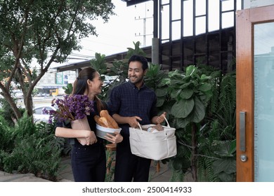 Multicultural small business owners startup carrying groceries outside cafe. Asian woman holding flowers and bread talking with Indian man with smiling. Friendly teamwork outdoor cafe restaurant - Powered by Shutterstock