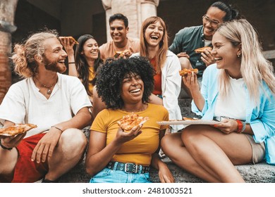 Multicultural smiling friends eating pizza sitting outside - Cheerful young people enjoying summer vacation together - Happy life style concept with guys and girls hanging out on a sunny day - Powered by Shutterstock