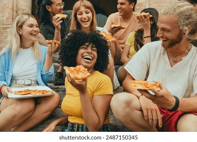 Multicultural smiling friends eating pizza sitting outside - Cheerful young people enjoying summer vacation together - Happy life style concept with guys and girls hanging out on a sunny day - Powered by Shutterstock