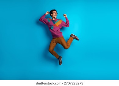 Multicultural stylish man energetically jumping in a trendy sweater on a vivid blue backdrop, showcasing creativity and enthusiasm