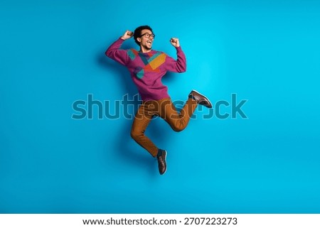 Multicultural stylish man energetically jumping in a trendy sweater on a vivid blue backdrop, showcasing creativity and enthusiasm
