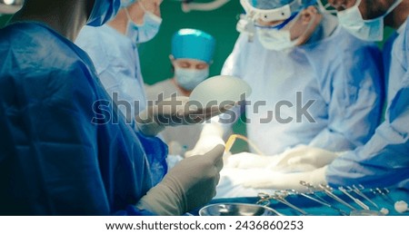 Multicultural team of professional plastic surgeons performs plastic surgery in modern private clinic. Surgeons and anesthesiologists work in operating room. Concept of medicine and treatment.