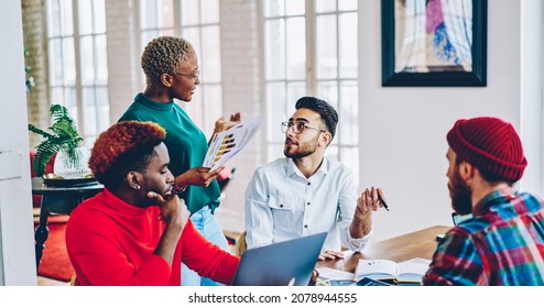 Multicultural team of young people discussing productive strategy of successful cooperation during briefing meeting in coworking, group of employees analyzing paper reports at desktop with netbook - Shutterstock ID 2078944555