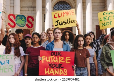 Multicultural teenagers holding a climate change protest in the city. Group of youth activists holding banners and placards while marching for climate justice and environmental sustainability. - Shutterstock ID 2189909481