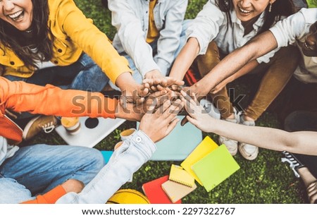 Multicultural university students stacking hands together in college campus - Young people hugging outside symbolizing unity and teamwork 