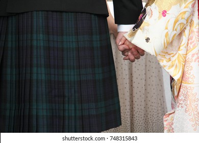 A Multicultural Wedding, With A Scottish Groom Wearing A Kilt, And A Japanese Bride In A Wedding Kimono, Holding Hands.