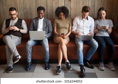 Multicultural young people using laptops and smartphones sitting in row, diverse african and caucasian millennials entertaining online obsessed with modern devices waiting in queue, gadget addiction - Shutterstock ID 1016244052