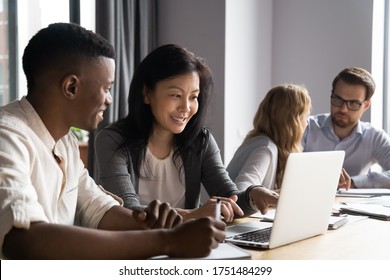 Multi-ethnic affiliates working on task together seated at desk in co-working, mature asian mentor teach new employee african guy, diverse mates having fun using laptop, learn corporate apps concept - Shutterstock ID 1751484299