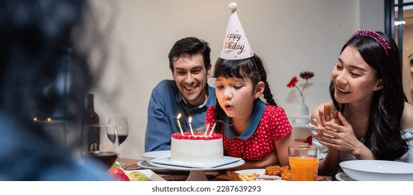 Multi-ethnic big family having a birthday party for young kid daughter. Lovely moment of diversity people singing a happy birthday song to little girl child then blowing candle on cake on dining table - Powered by Shutterstock