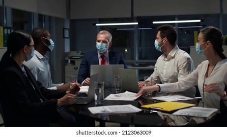 Multiethnic Business Partners In Safety Mask Gather In Board Room For Meeting. Diverse Businesspeople Wearing Protective Mask Discuss Contract In Conference Room Late In Evening