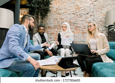 Multiethnic Business People On The Meeting In Office. Arabian Business Lady In White Hijab Using Financial Document With Graphs Talking To Her Male And Female Partners About The Results Of Research