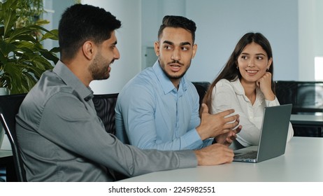 Multiethnic business team three office workers managers discus project online crypto currency brainstorm with laptop computer at workplace. Multiracial coworkers group talk about corporate software