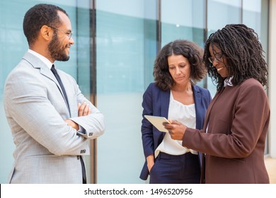 Multiethnic business team watching and discussing project data on tablet. Business man and women sanding near office, using tablet together, talking and laughing. Communication concept - Shutterstock ID 1496520956