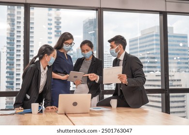 Multiethnic business team wearing face mask during business meeting in new normal office. Diverse corporate colleagues brainstorming with technology device and business paperwork - Powered by Shutterstock