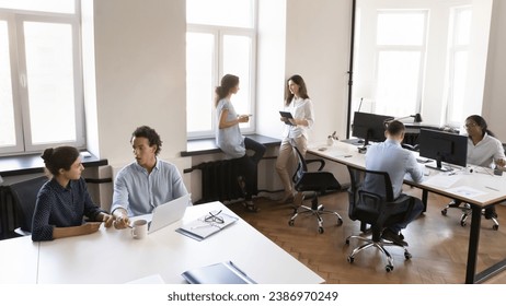 Multiethnic business team working in small office space, using laptop computer, cooperating on project, common tasks, talking at shared workplace tables. Modern rental co-working space - Powered by Shutterstock