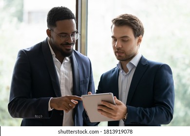 Multiethnic businessmen look at tablet screen discuss business project together. Smiling diverse multiracial male colleagues brainstorm cooperate on pad in office. Technology, teamwork concept.