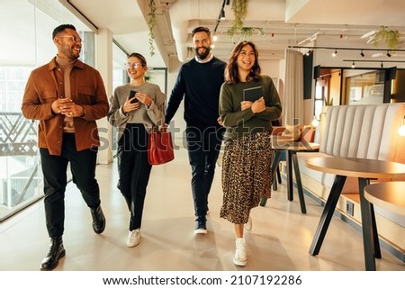 Multiethnic businesspeople walking through a modern office in the morning. Team of happy businesspeople smiling cheerfully. Group of diverse entrepreneurs working together in a co-working space.