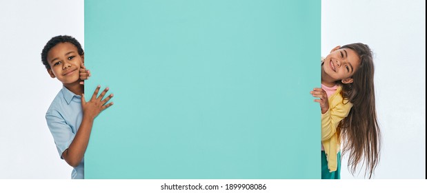 Multi-ethnic children peeking from behind an empty turquoise wall. Empty space for text with kids