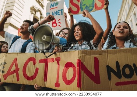 Multiethnic climate activists protesting with banners and a megaphone. Vibrant young people marching against global warming and pollution. Group of teenagers joining the global climate strike.