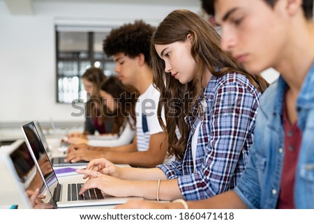 Multiethnic college students sitting in a classroom studying on laptop during class. Group of guys and girls using laptop during computer lesson. Lifestyle and mobile communication technologies.