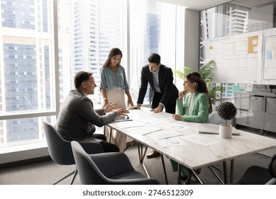 Multiethnic company managers startup developers team with middle aged leader boss gather around boardroom table brainstorming insights creating plans reviewing project materials in modern urban office