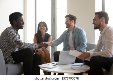 Multi-ethnic Company Staff Meet Client Boss Shake Hands Express Respectful Attitude Start On Finish Effective Negotiations Seated On Cozy Sofa In Modern Office Room, Business Gesture Etiquette Concept