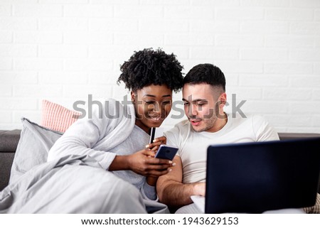 Multiethnic couple in bed in pijamas looking at notebook and enjoy in morning