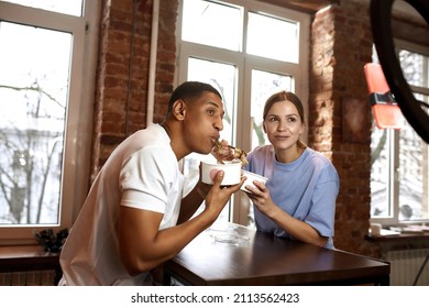 Multiethnic Couple Eat Noodles During Make Eat Fast Food Video Challenge On Smartphone. Video Blogging. Black Man And Caucasian Woman Of Generation Z Create Content For Social Networks At Home Kitchen