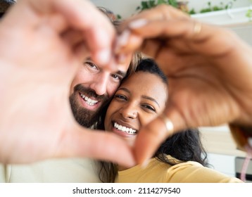 Multiethnic couple at home making a heart shape with their hands.	 - Shutterstock ID 2114279540