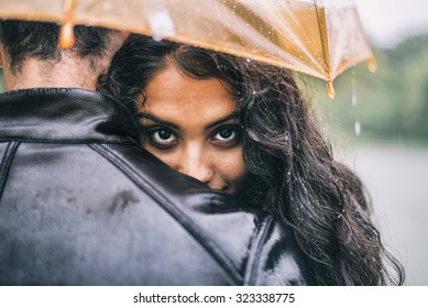 Multiethnic Couple Of Lovers Hugging Under The Umbrella On A Rainy Day -  Man And Woman On A Romantic Date Under The Rain, Boyfriend Hugs His Partner To Protect Her