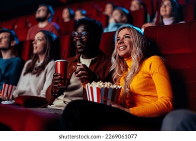 A multiethnic couple is in the movie theater, enjoying drinks and popcorn and watching a movie. - Powered by Shutterstock