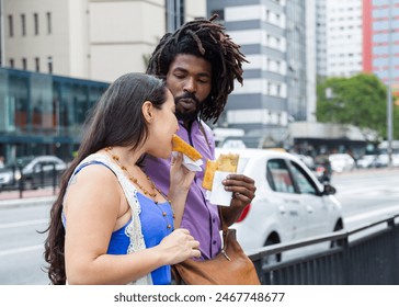 Multiethnic couple sharing in the streets brazilian food known as Pastel - asian recipe. - Powered by Shutterstock