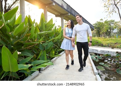 Multiethnic Couple Walking Distracted For A Path Of An Urban Park During Sunset