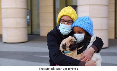 Multiethnic couple wearing safety mask meeting after long time hugging near airport with pug dog. African woman with pet dog greeting caucasian boyfriend outside airport building